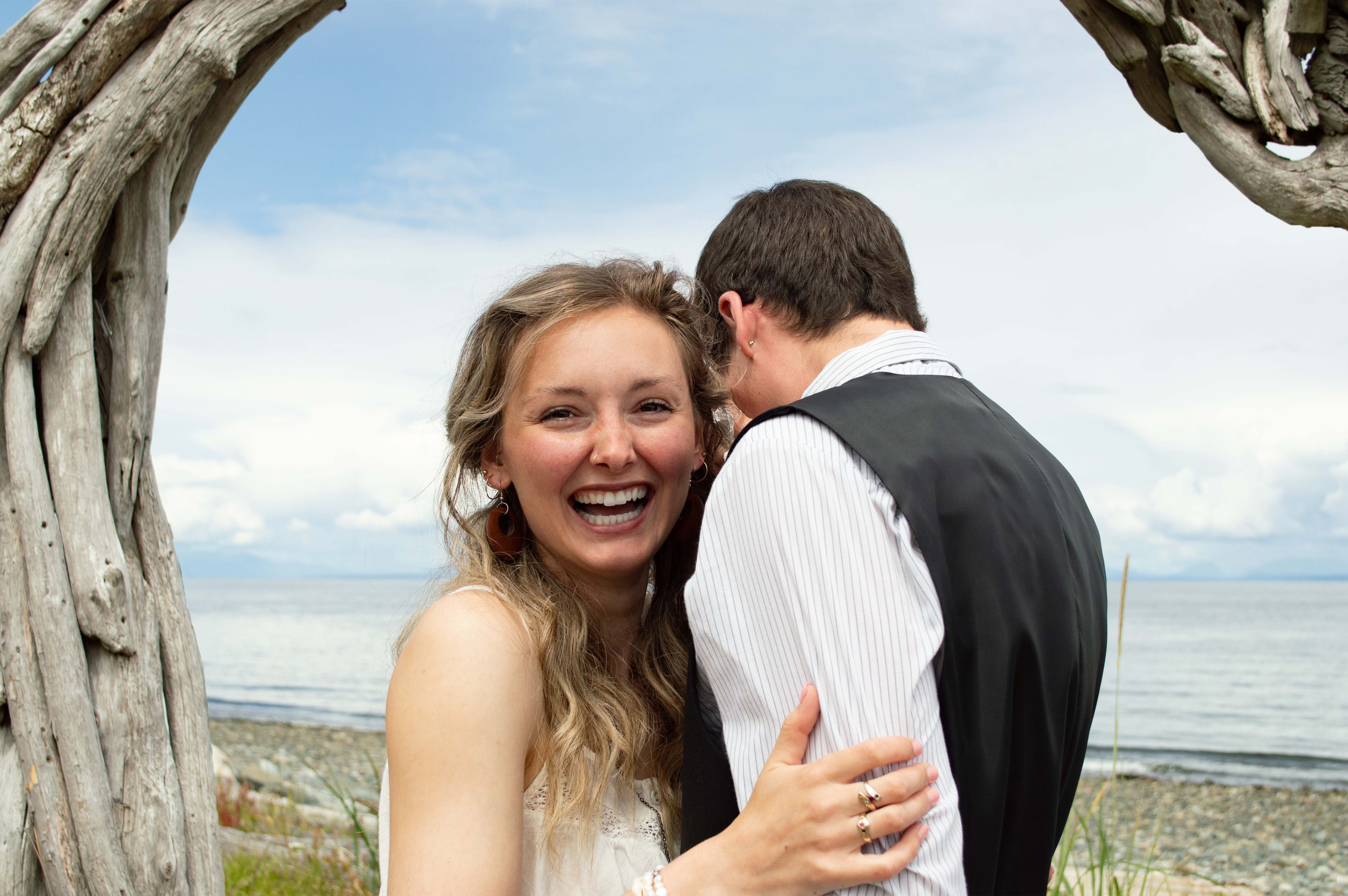 A bride smiling at toward the camera while hugging her groom.